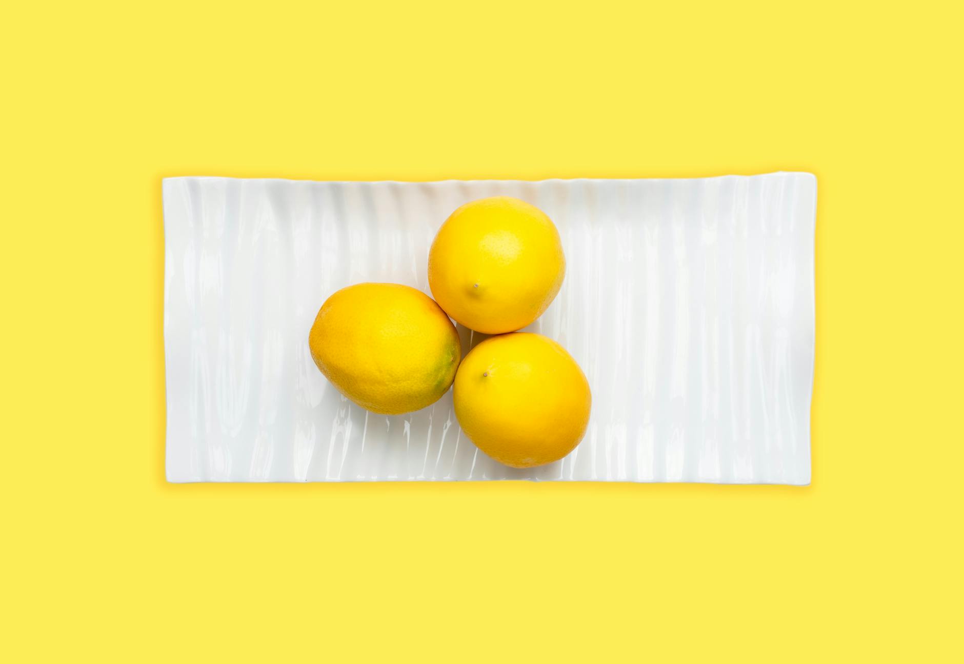 Fresh lemons arranged on a white plate with a vibrant yellow background, representing openness and freshness in intimate communication