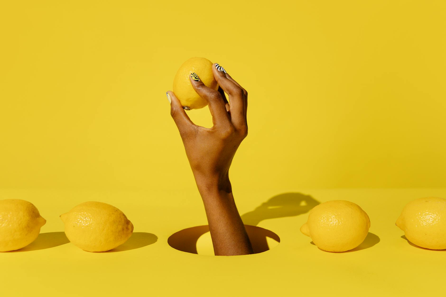 Hand holding a fresh lemon against a vivid yellow background, symbolizing accessible pleasure