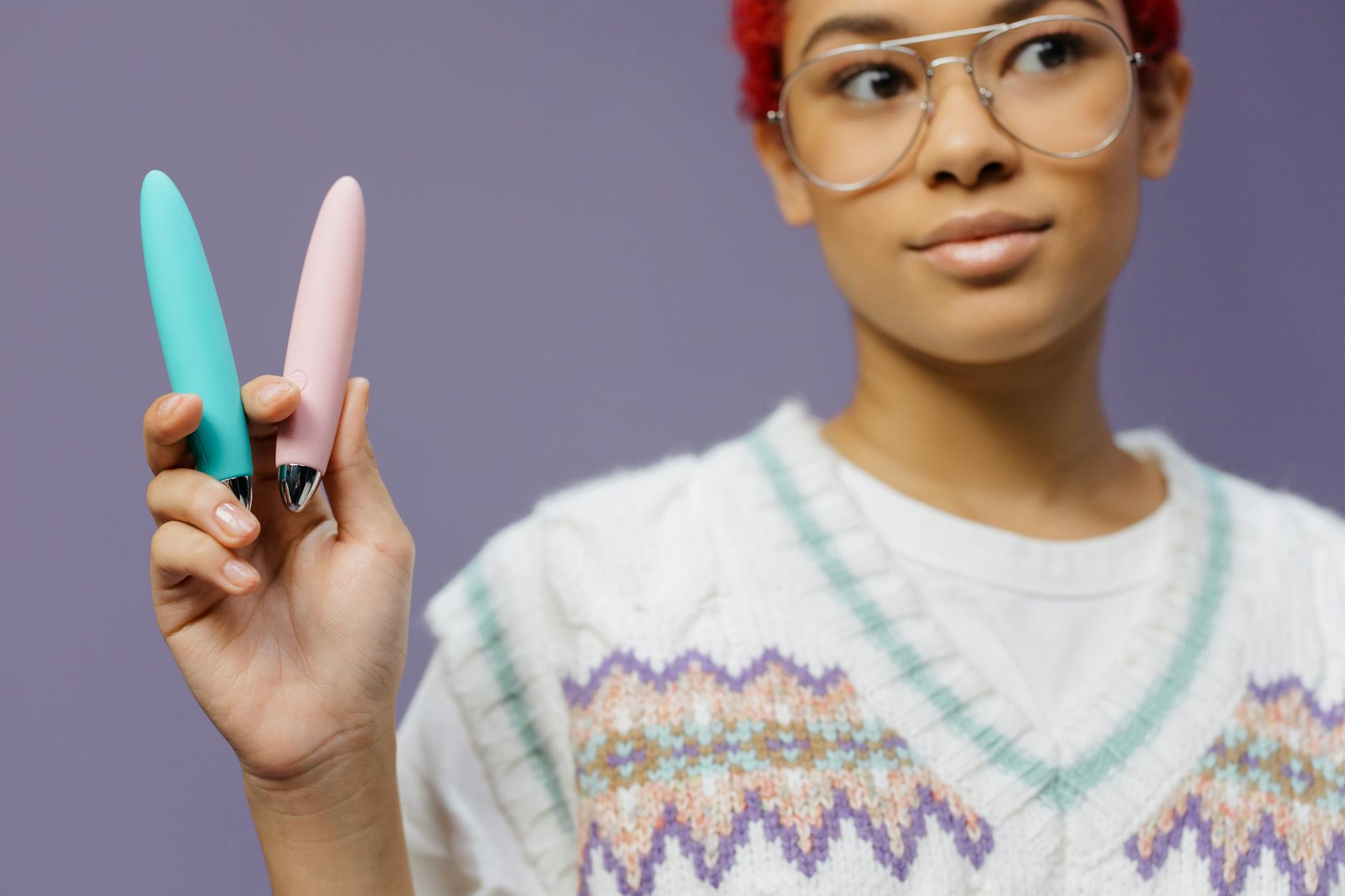 Hands holding colorful clitoral vibrators against a purple background