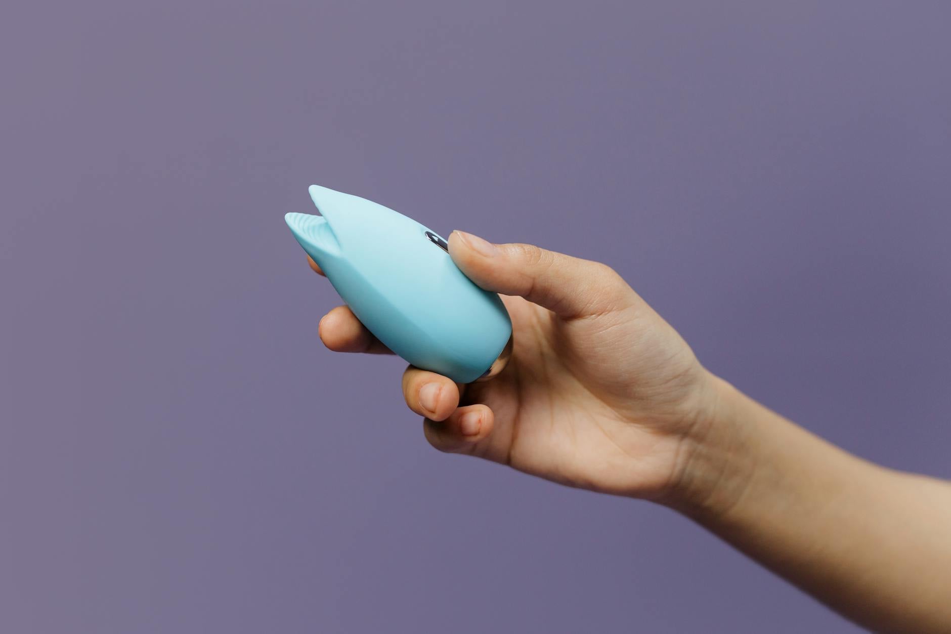 A hand holding an orange vibrator against a minimalistic purple backdrop, showcasing modern sensuality and gentle exploration.