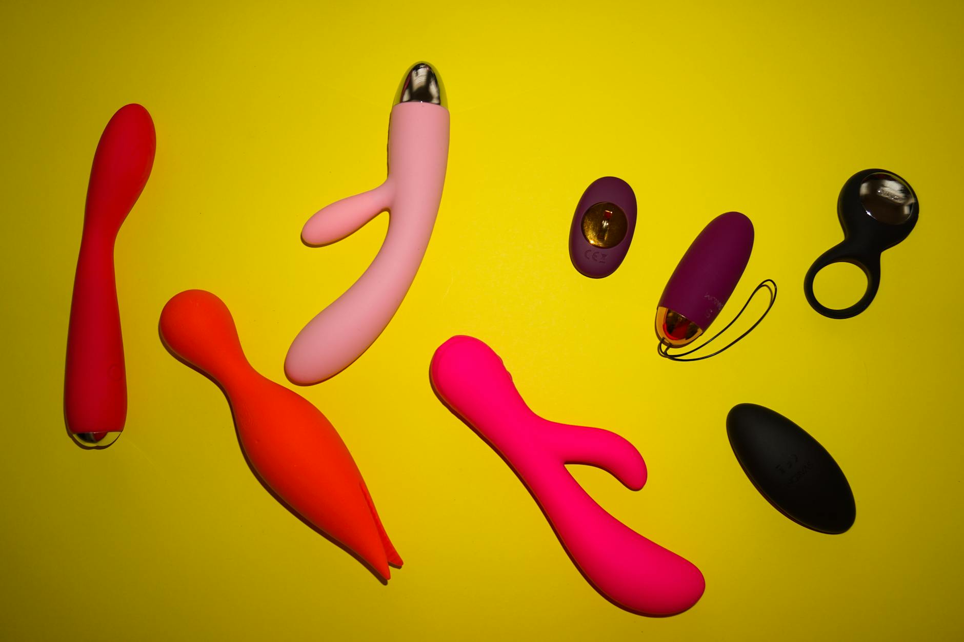 Collection of colorful clitoral vibrators and adult toys arranged on a bright yellow surface